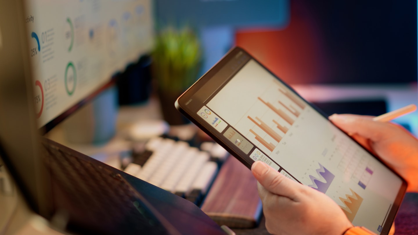 Person analyzing business charts on a tablet at a desk.